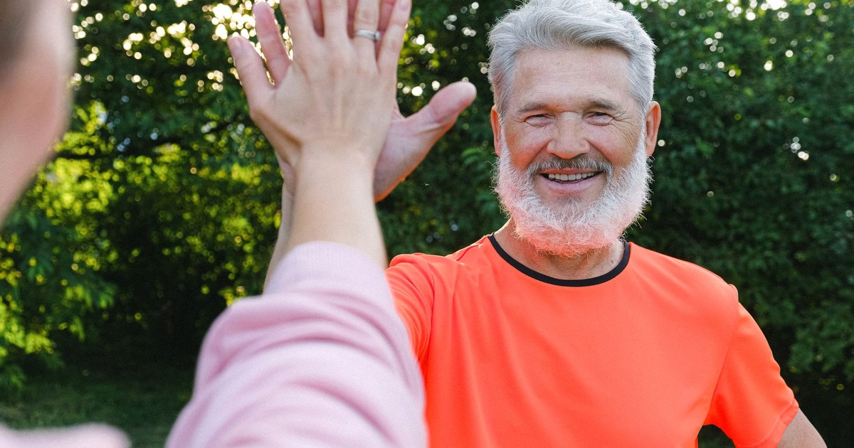 Cheerful aged man in bright clothes smiling and giving high five to friend in sunny day