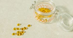 One Common Vitamin Could Lower Toxic Alzheimer's Proteins, Research Suggests Close-up of open glass jar filled with yellow health capsules on light surface.