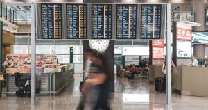 Blurred motion of travelers in a modern airport terminal with departure screens and a prominent clock.