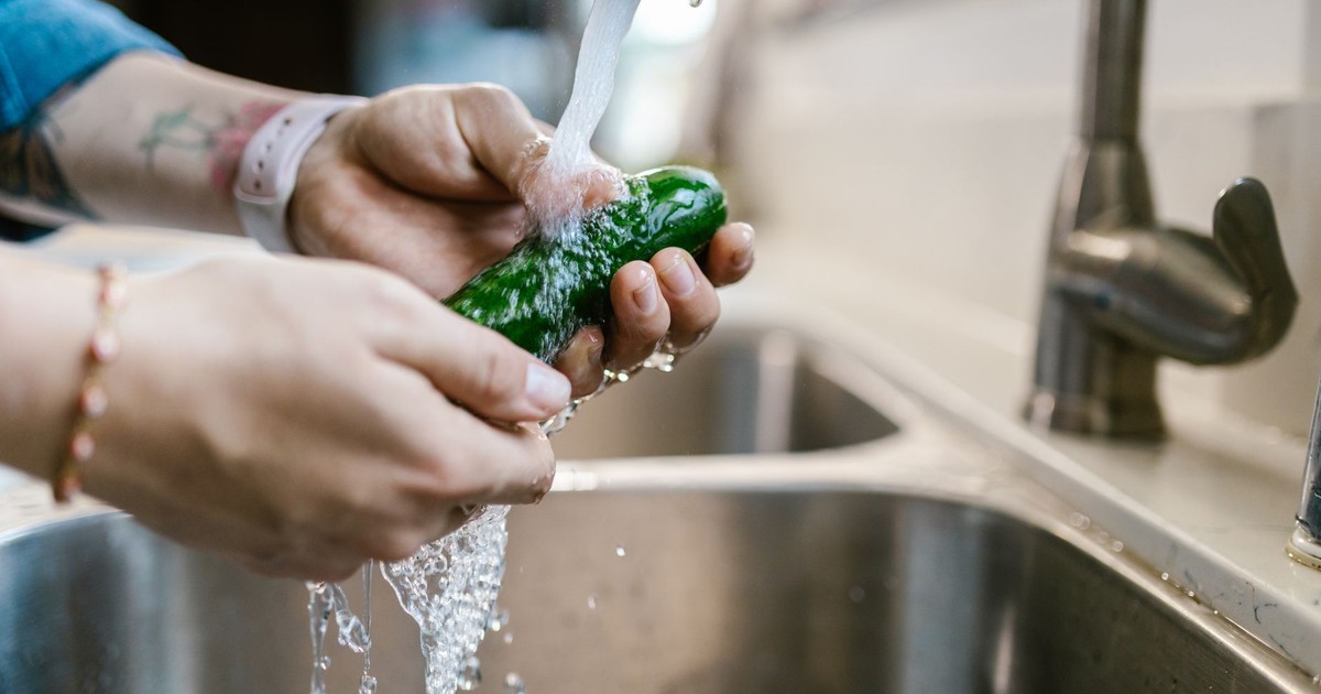 Close-up of hands washing a green vegetable under a kitchen faucet, emphasizing cleanliness and food preparation.