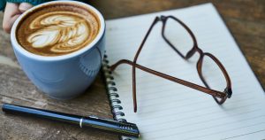 People Who Drink Popular Morning Staple Had a 47% Lower Risk of a Specific Kind of Cancer, New Study Finds Cozy workspace featuring latte art, notebook, and glasses, perfect for creative thoughts.