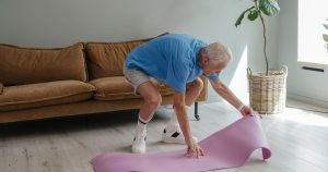 An elderly man sets up his yoga mat indoors, embodying a healthy lifestyle.