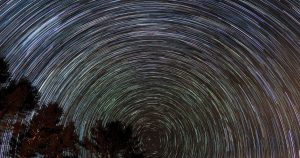 Mesmerizing long exposure shot capturing star trails over silhouetted trees, showcasing the beauty of the night sky.