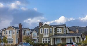 Picturesque suburban neighborhood with modern houses and parked cars under a partly cloudy sky.