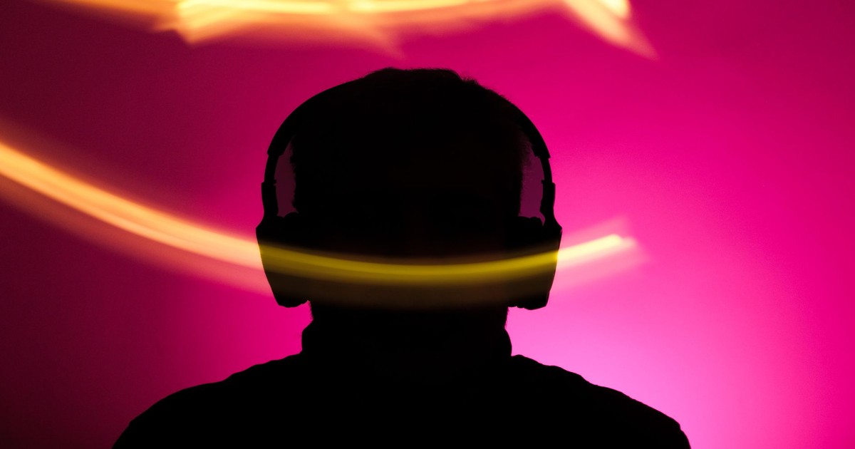 Silhouette of person with headphones against vibrant pink background and dynamic light streaks.