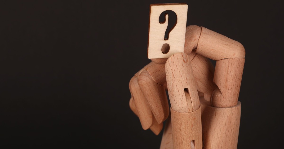 Close-up of a wooden mannequin hand holding a block with a question mark, emphasizing curiosity.