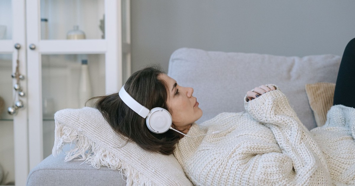 Woman lying on a sofa, wearing headphones, relaxed and cozy indoors, capturing a moment of tranquility.