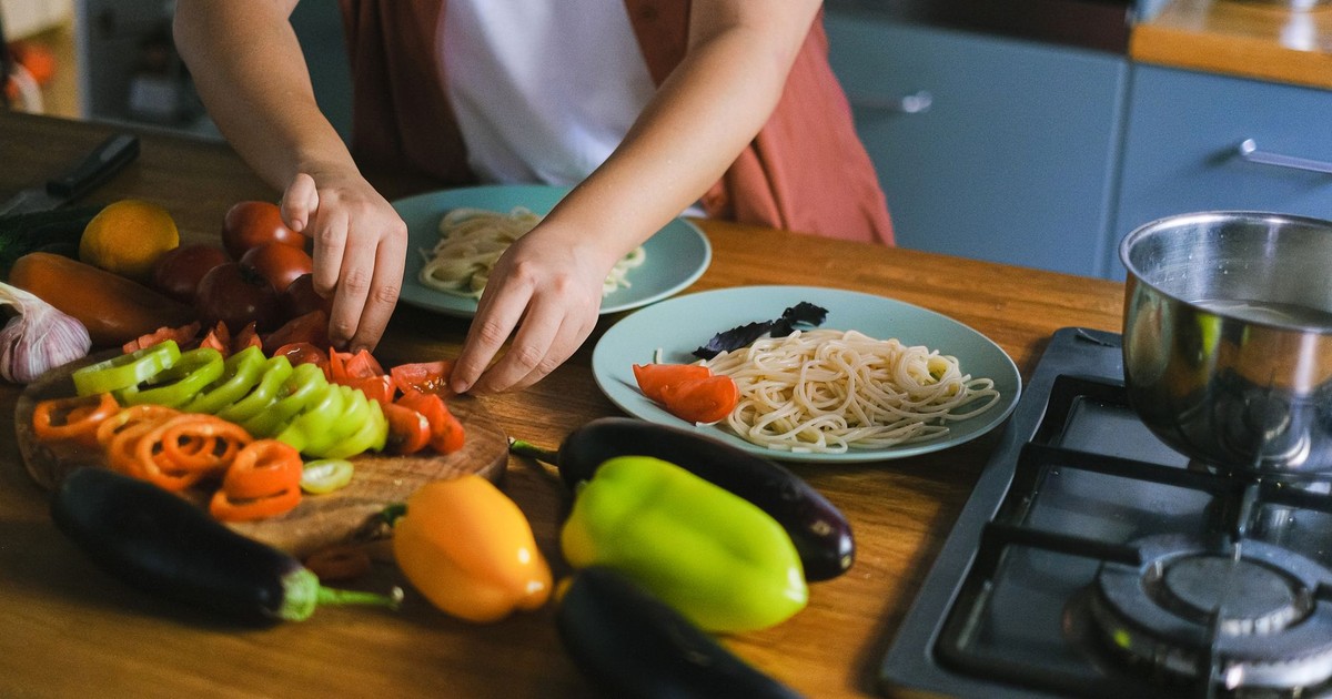 Woman arranging fresh vegetables and pasta on plates in a kitchen setting.