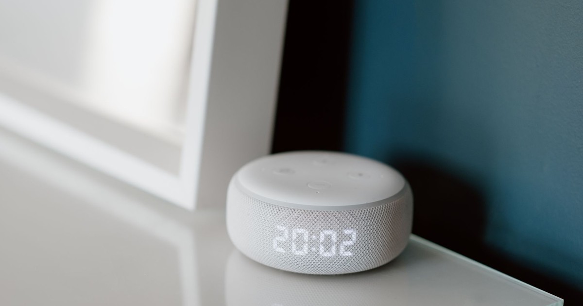 Close-up of a smart speaker with an illuminated 20:02 LED clock display on a desk.