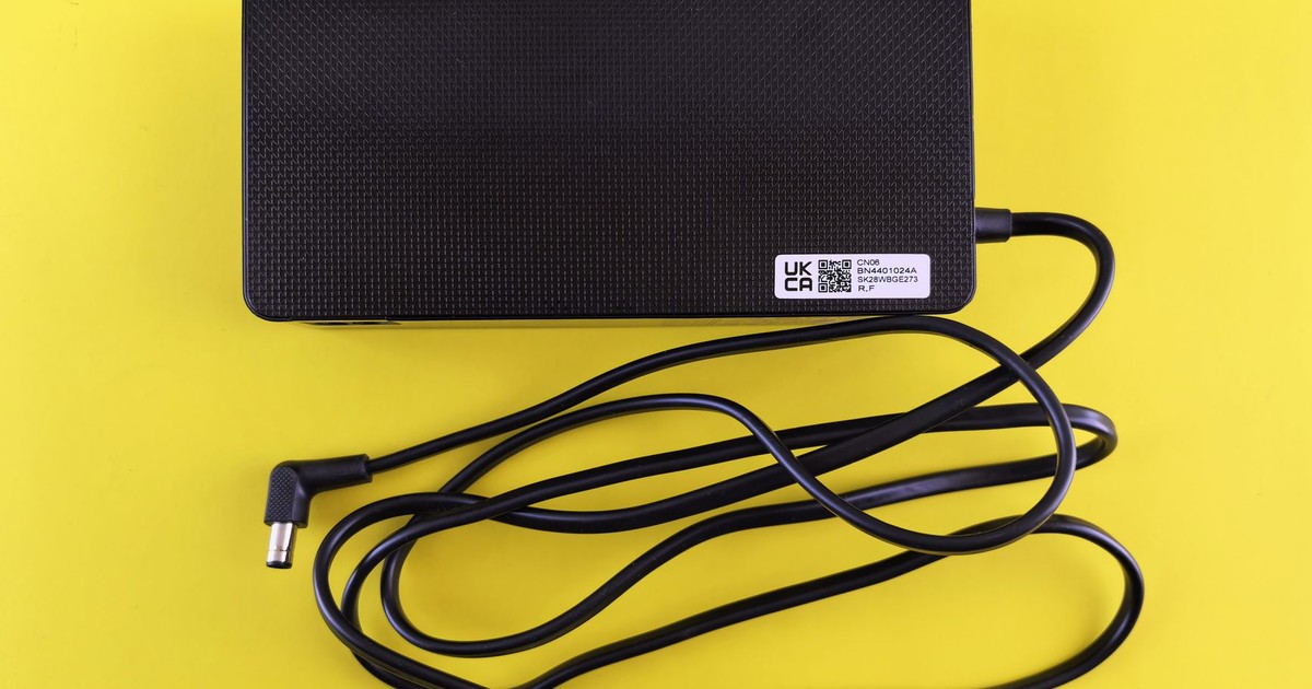 A black power adapter with cord on a vibrant yellow background, showcasing electronics.