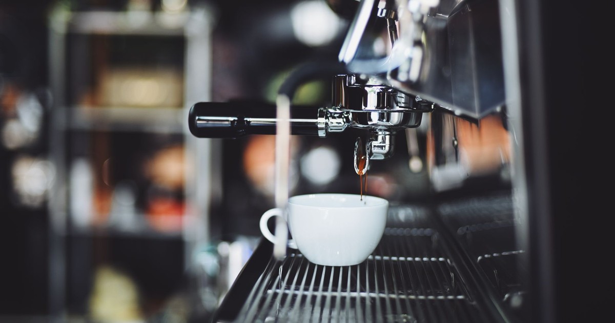 Close-up of espresso machine brewing coffee into a white cup in a cafe setting.