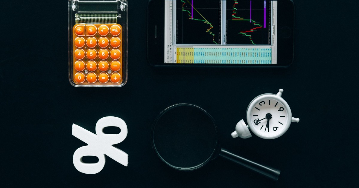 Top view of business tools including a calculator, smartphone with charts, magnifying glass, and clock on black background.