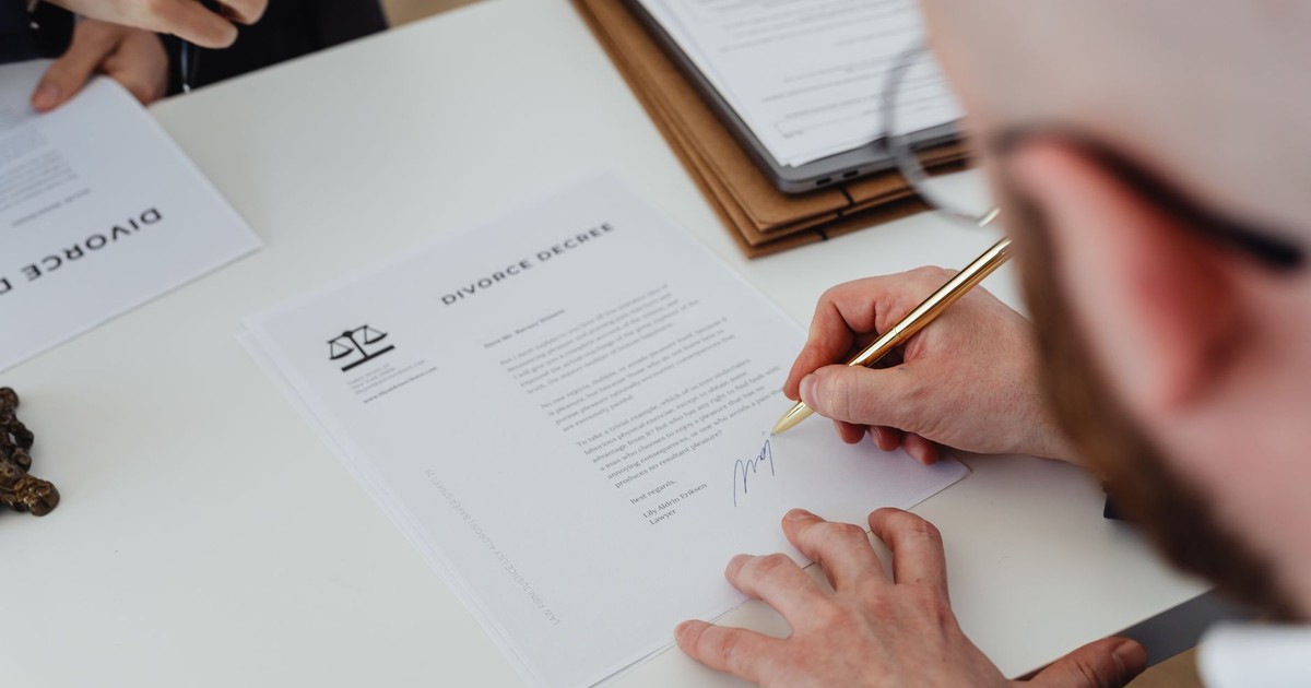 Close-up of a person signing a divorce decree on a desk.