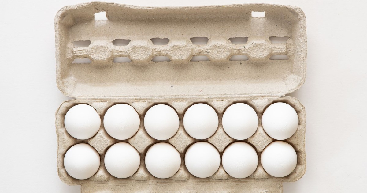 Minimalist flat lay of white eggs in a carton tray, perfect for culinary or health concepts.
