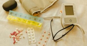 6 Blood Pressure Medication Side Effects Men Need to Know About Flat lay image of healthcare essentials including a blood pressure monitor, pills, and eyeglasses on a white surface.