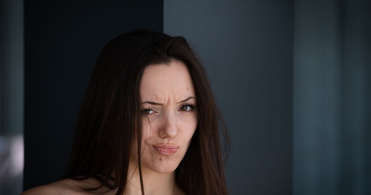 Captivating portrait of a woman with long brown hair and expressive face against a gray background.
