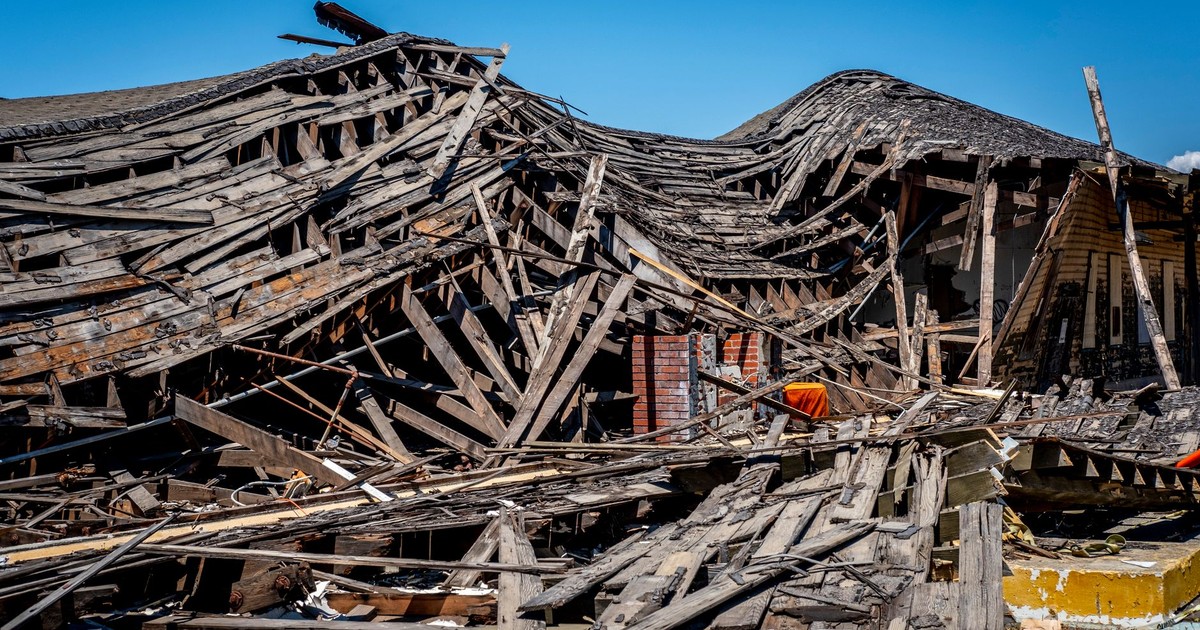 A dramatic view of a destroyed wooden building after a catastrophe, showing debris and structural failure.