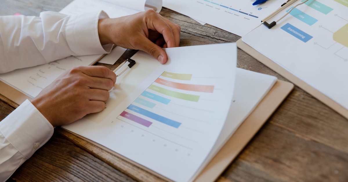 Close-up of hands reviewing business report with colorful charts and graphs on a wooden desk.
