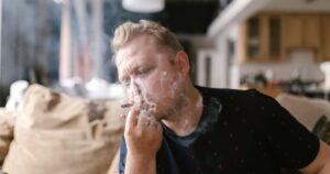 A Cannabis-Tobacco Combination May Triple Your Schizophrenia Risk Adult man enjoying a smoke indoors, surrounded by a casual home setting.