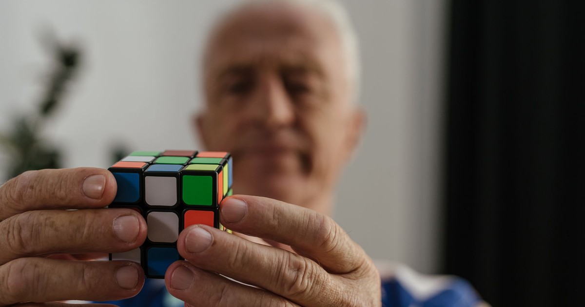 A senior adult man solving a Rubik's Cube, focusing on the puzzle with determination.