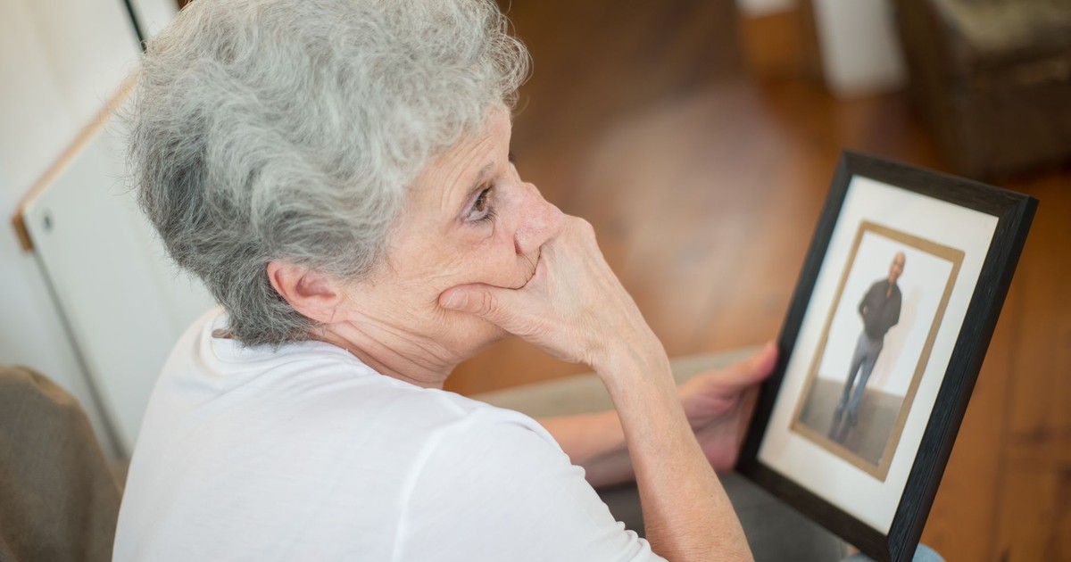 Thoughtful elderly woman with a framed photo, reflecting on memories.