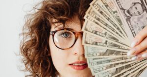Caucasian woman with eyeglasses holding US dollar bills, highlighting finance and savings.