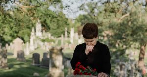 Type of Grief No One Talks About A woman in black paying her respects at a grave, holding flowers in a serene cemetery.
