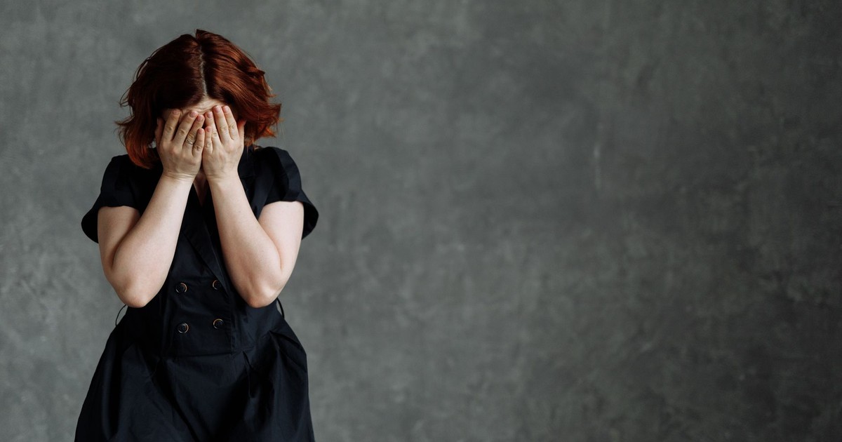 A woman in a black dress expressing emotion against a concrete backdrop, highlighting themes of sadness and stress.