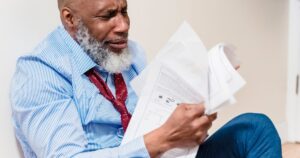 Colorado's Insurance Crisis: What's Happening and What You Should Do Now African American man in distress with paperwork, sitting against a wall indoors.