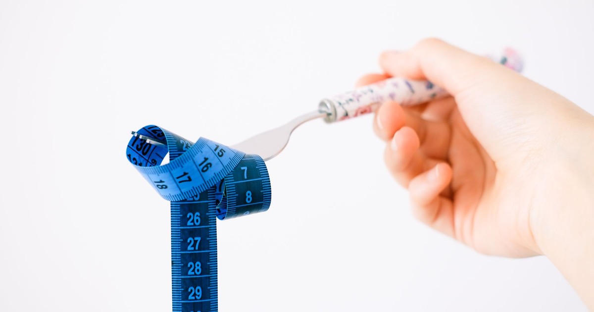 A hand holding a fork wrapped with a blue measuring tape suggesting diet or weight management.
