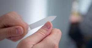 Detailed close-up of a person's hands filing nails with a nail file indoors.