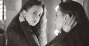 8 Traits of Malignant Narcissism That People Who Lack Empathy & Crave Control Often Share A woman contemplating her reflection in a lit vanity mirror indoors.