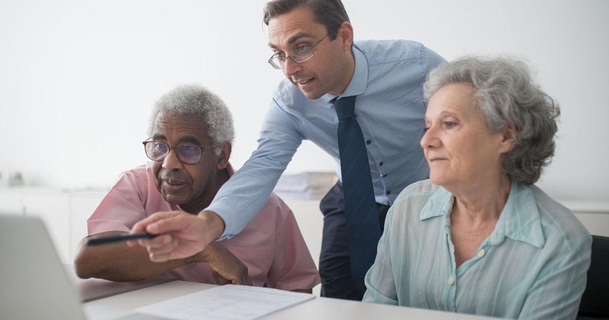 A business consultant explaining financial options to senior clients, using a laptop for illustration.