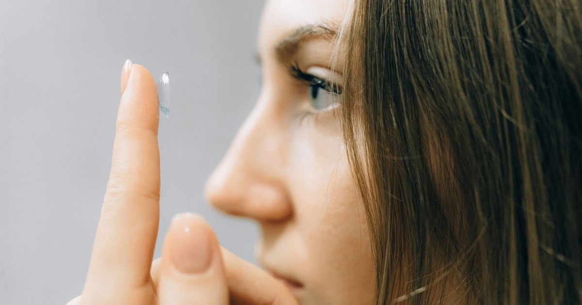 A young woman focuses intently as she applies a contact lens, close-up shot highlighting her eye and careful fingers.