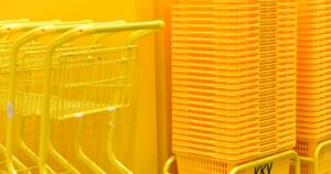 Stack of vibrant yellow shopping carts and baskets in a retail store aisle.