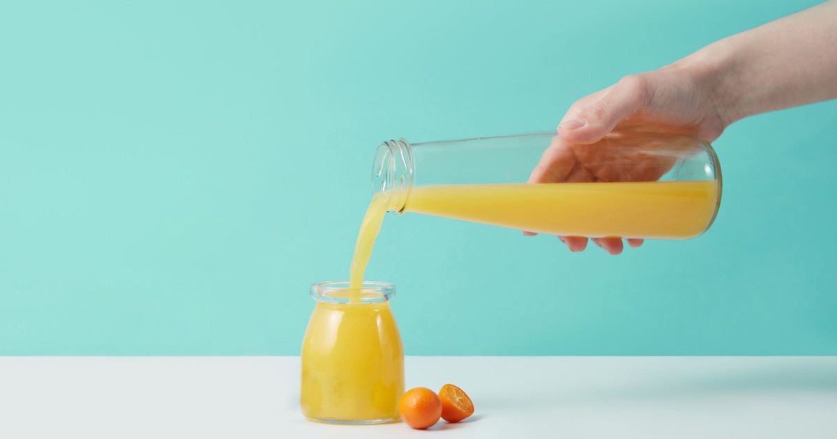 Refreshing orange juice being poured from a glass pitcher into a jar, set against a turquoise background.