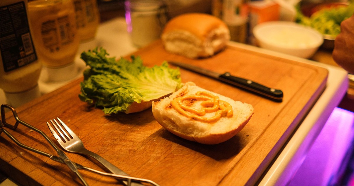 Close-up of sandwich preparation with fresh lettuce and mayonnaise on a wooden board.