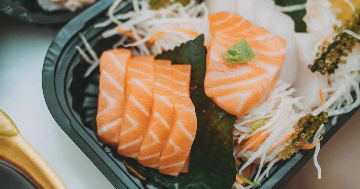 Close-up of fresh salmon sashimi served on a black plate with wasabi garnish.