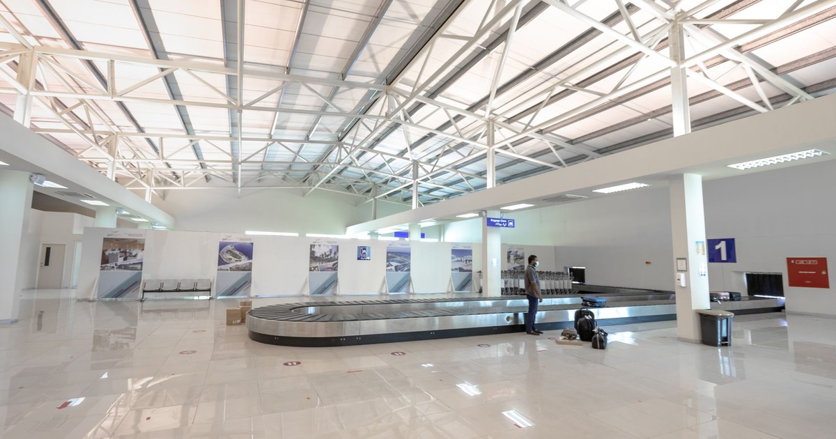 A modern and empty airport baggage claim area with a traveler waiting.