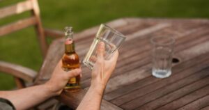 From above of crop anonymous male sitting at wooden table with glass mug and beer