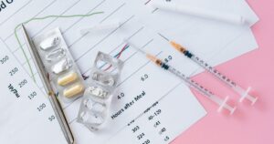 11 Everyday Foods That Can Interfere With Blood Thinners Flat lay of medicines, syringes, and a blood glucose chart on a pink surface, representing health management.