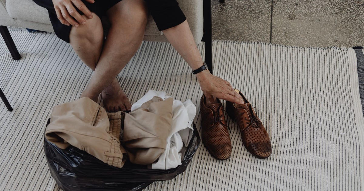 A person sorts through clothes and shoes while sitting on a striped carpet indoors.