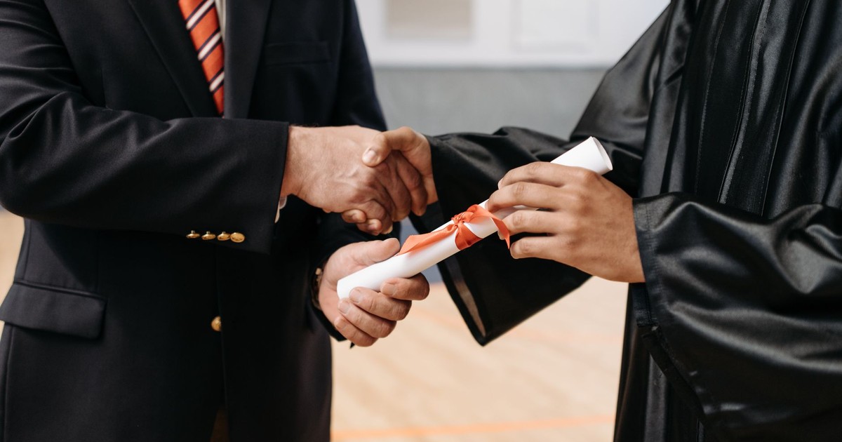 Close-up of a graduate receiving diploma during a graduation ceremony handshake.