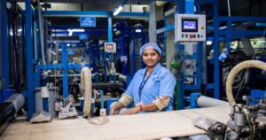 200 Economists — Including Nobel Winners — Warn AI Job Losses Are Coming Smiling female worker in a modern textile factory, showcasing the industrial workspace.