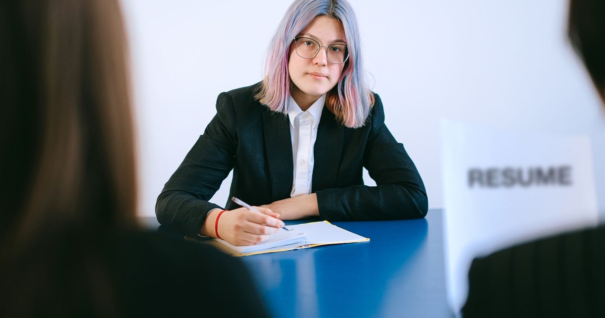 A young woman with dyed hair takes notes during a job interview.