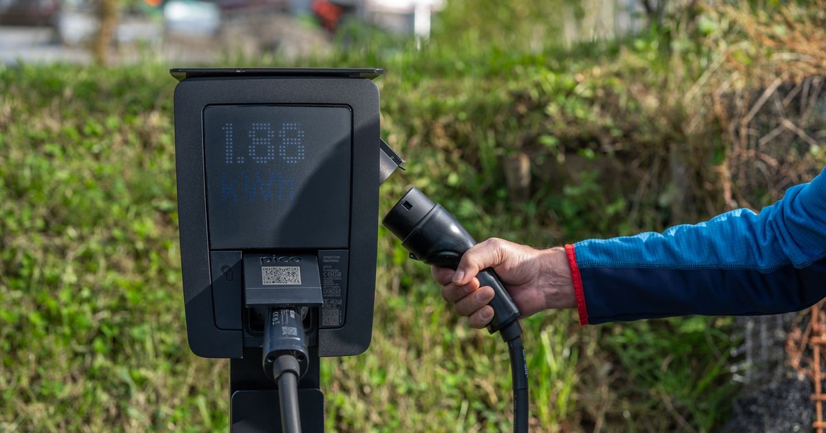 An outdoor electric car charging station with a hand holding a charging cable.