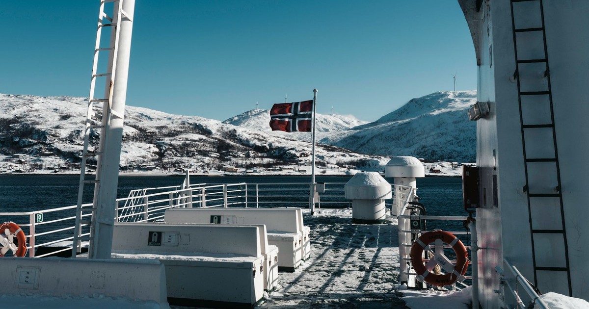 Scenic view of a ship deck with a Norwegian flag and snowy mountains in winter.