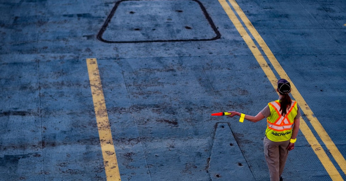 A BC Ferries worker directs traffic on the ferry deck, wearing a high-visibility jacket.