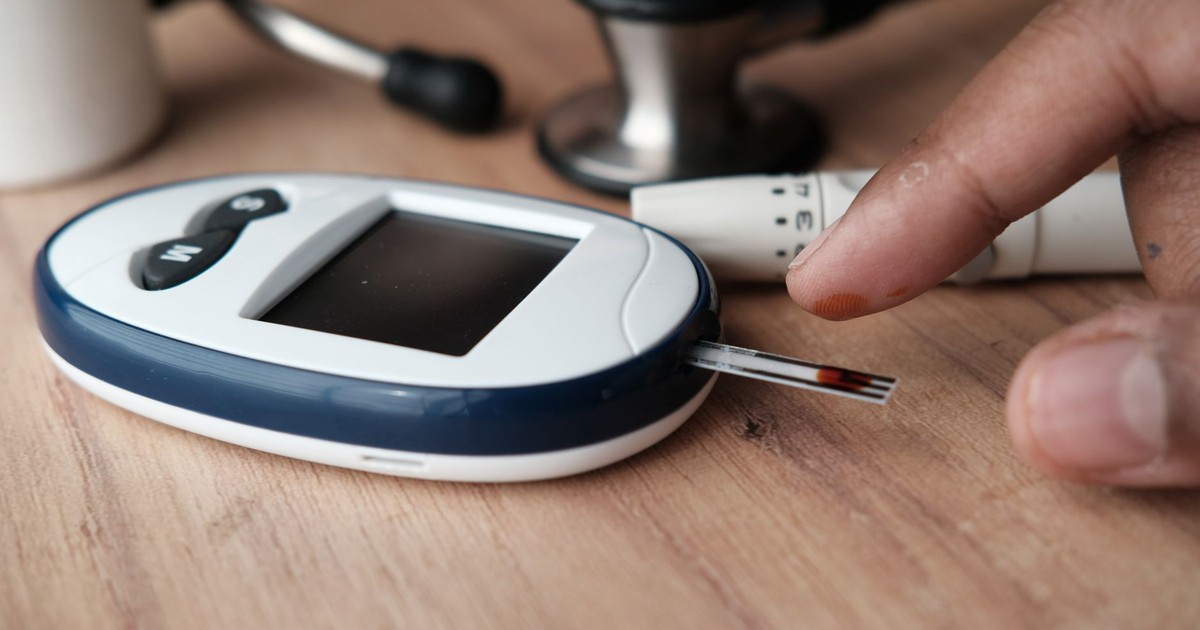 Close-up image of a glucometer checking blood sugar level with a finger pricking device nearby.