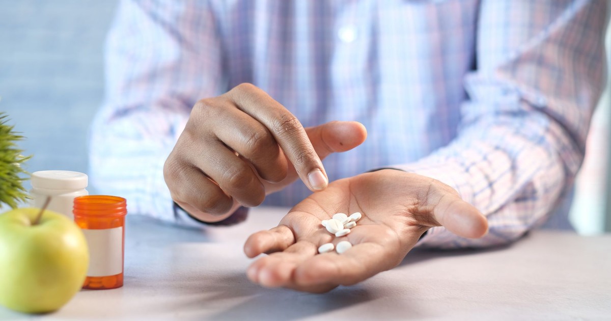 Close-up of a man's hands holding and pointing at white pills next to a prescription bottle.